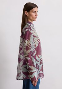 Long-sleeve shirt in sheer maroon fabric with light green floral pattern, featuring a collared neck and buttoned cuffs.