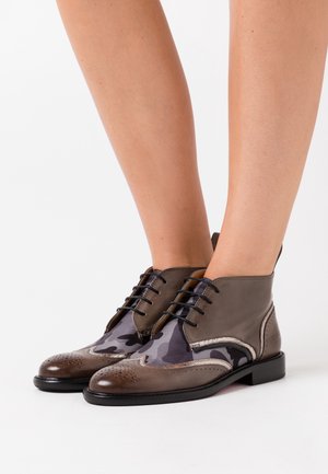 Ruske nahkasaapaat nilkkamitoilla, joissa on kamouflagekuvio, sileä päällinen, rei'itetty kärki, musta pohja ja nauhakiinnitys.