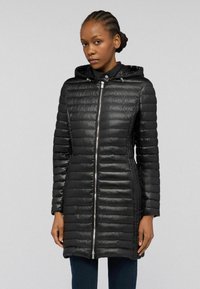 Svart vadderad jacka med huva, utrustad med en metallblixtlås, quiltad struktur och sidofickor. Materialet har en glänsande yta.