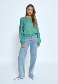 Mint green oversized sweater with wide sleeves, paired with light blue straight-leg jeans and embellished silver flats.