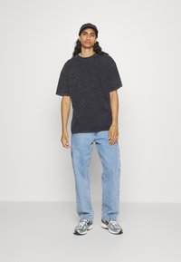 Sort oversized T-shirt med korte ærmer, falmet struktur, parret med lyseblå straight-leg jeans og grå sneakers. Sort kasket på hovedet.