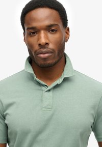 Polo shirt verde chiaro realizzato in tessuto morbido, con colletto a piega e due bottoni al collo. Texture liscia con dettagli minimi.