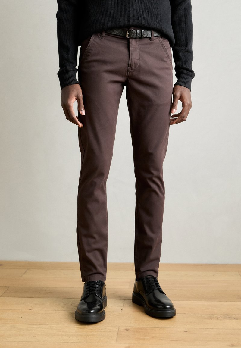 Καφέ κοτλέ παντελόνι με στενή εφαρμογή, που διαθέτει πλαϊνές τσέπες και φερμουάρ. Συνδυάζεται με μαύρα δερμάτινα παπούτσια και μαύρη ζώνη.