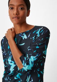 Zwarte jurk met blauwe en turquoise abstracte patronen, met een bootnek en driekwart mouwen. Glad, lichtgewicht stof.