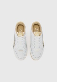 Chaussures de sport en cuir blanc avec des accents beige, semelles texturées, perforations sur l'avant-pied et un logo Puma sur la languette et le côté.