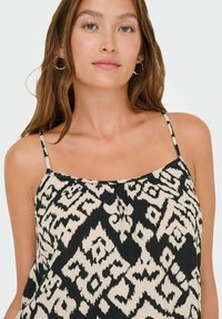 Zwart en beige gepatternde top met dunne bandjes, met een abstract ontwerp en een vloeiende, lichte textuur.