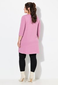 Rosa Tunika-Oberteil mit Dreiviertelärmeln, kombiniert mit schwarzen Leggings und weißen Stiefeletten. Glatter Stoff und entspannte Passform.