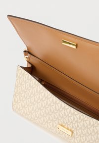 Portefeuille Michael Kors beige et marron avec motif monogramme, plaque logo dorée et compartiment zippé à l'intérieur du rabat.