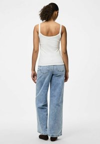 Top sin mangas blanco con canalé y tirantes finos, combinado con jeans de pierna ancha de color azul claro. El fondo es blanco liso, destacando el conjunto.