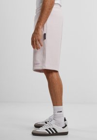 Lys rosa bomullsshorts med snøring i livet, sidelommer og brodert "Forbudt"-merke. Kombinert med svarte og hvite joggesko.