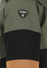 Hoodien har et farveblokeret design med grønne, sorte og brune sektioner. Den inkluderer et sort ZigZag-logo-patch på den øverste venstre side.