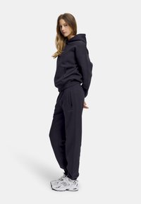 Mørkegrå hettegenser med kengurulomme og matchende joggebukser. Glatt stoff med en avslappet passform. Hvite sneakers kompletterer antrekket.