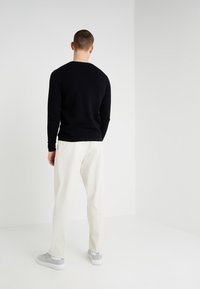 Maglione lungo a maniche lunghe di colore nero con un motivo tessuto, abbinato a pantaloni larghi di colore chiaro e sneaker grigie.