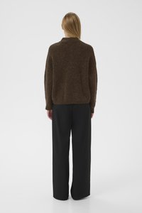 Suéter marrón texturizado con un corte relajado, que cuenta con mangas largas y un cuello poco profundo. Combinado con pantalones negros de corte holgado.