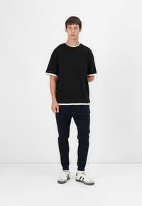 Schwarzes Kurzarm-T-Shirt mit weißem Saum; kombiniert mit navyblauen Slim-Fit-Jogginghosen und weißen Sneakers mit grauen Akzenten. Einfaches, lässiges Outfit.