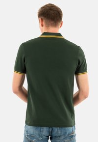 Donkergroene polo-shirt met een geel gestreepte kraag, korte mouwen en een gladde textuur, van achteren getoond op een persoon.