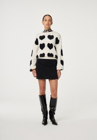 Trui met fuzzy zwarte harten op een crèmekleurige achtergrond, gecombineerd met een zwarte corduroy mini-rok en hoge glanzende zwarte laarzen.