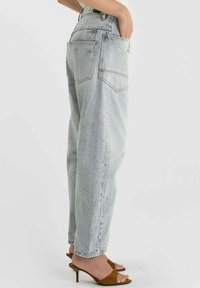 Jean gris clair taille haute avec une coupe décontractée, doté de deux poches arrière et d'ourlets retroussés. Associé à des sandales à talons marron.