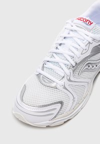 Scarpa sportiva bianca con parte superiore in rete e accenti argento. Presenta una punta arrotondata e un colletto imbottito, chiuso con lacci bianchi. Dettaglio del logo rosso.