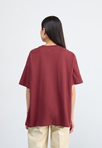 T-shirt court à manches courtes bordeaux avec une coupe décontractée. En matière coton, col rond et détails de couture discrets au dos.