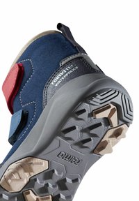 Wasserfeste Wanderschuhe mit einem Obermaterial aus Marineblau und Rot, einer robusten grauen Gummisohle und einer strukturierten Profilierung für besseren Grip. Mit einem Klettverschluss ausgestattet.