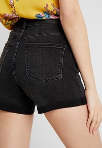 Högmidjade svarta denimshorts med fransad fåll, två bakfickor och ljusa sömnadsdetaljer som visar på en skräddarsydd passform.