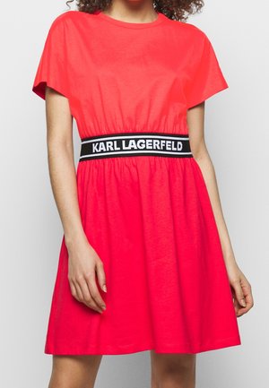 Vestido de manga corta y corte en línea A en tela de color rosa brillante. Cuenta con una cintura elástica negra con el texto "KARL LAGERFELD" en blanco. Textura suave.