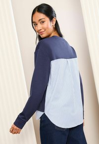 Felpa blu navy con una parte posteriore a strisce blu e bianche, dotata di un orlo rotondo e maniche lunghe. Tessuto morbido con una vestibilità comoda.