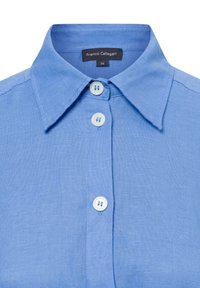 Himmelblaues Leinenhemd mit spitzem Kragen, ausgestattet mit weißen Knöpfen und einem Etikett, auf dem "Franco Callegari" und Größe 36 steht. Weiche Textur.