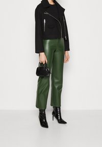 Veste noire courte avec fermetures éclair argentées, pantalon en simili cuir vert et bottines noires à talonsPointus. Petit sac à main noir avec un fini texturé.