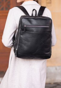 Juuri musta nahkareppu, jossa on sileä pinta, etupuolella vetoketjullinen tasku ja säädettävät hihnat. Suorakulmainen muoto, minimalistinen muotoilu.