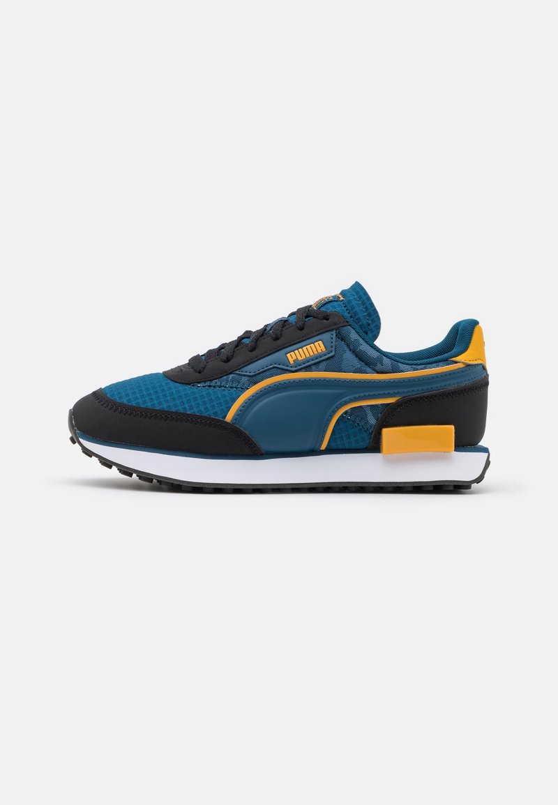 Basket Puma bleue et noire avec des accents jaunes et une semelle blanche, vue de côté sur un fond gris clair uni.