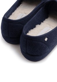 Marineblauwe vilt slippers met een zachte beige voering, afgeronde vorm en klein zilveren accentdetail. Ontworpen voor comfort en warmte.