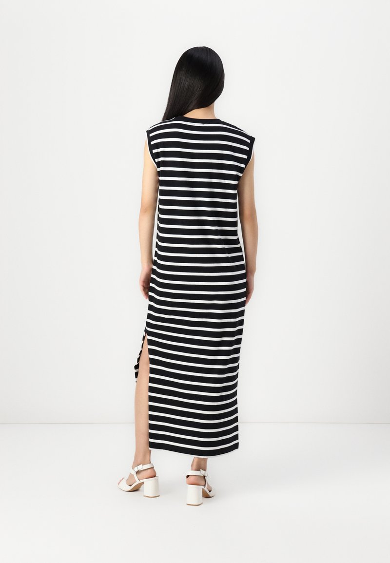 Gestreiftes ärmelloses Kleid in Schwarz und Weiß mit seitlichen Schlitzen, aus weichem Stoff, knöchellang, mit lockerer Passform. Weiße Blockabsatzsandalen.