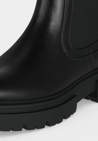 Bottine en cuir noir avec panneau latéral élastique et semelle épaisse à crampons pour adhérence et durabilité.