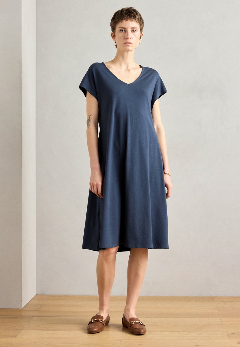Navy blue cotton dress with short sleeves, V-neckline, relaxed fit, and knee-length skirt. Worn with brown loafers. Smooth texture.