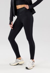 Sorte leggings med en tettsittende design, som har matte og glatte paneler, sammen med sølv- og svarte sneakers.