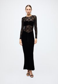 Black dress featuring a lace bodice with long sleeves, a velvet skirt, and ruching details along the sides and waist for a fitted silhouette.