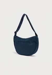 Tamnoplava torba za rame izrađena od glatke tkanine, ima zakrivljeni oblik, podesivi remen s logotipom i džep na prednjoj strani s patentnim zatvaračem.