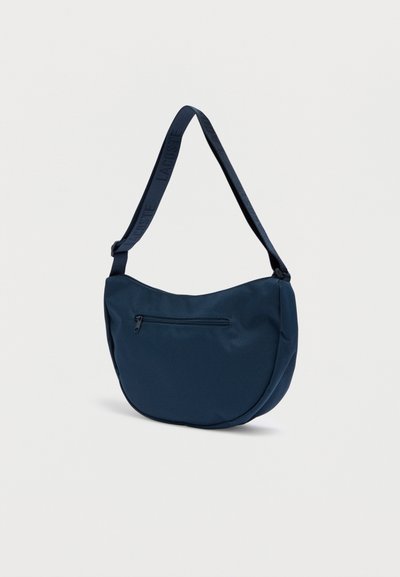 Sac à bandoulière bleu marine en tissu lisse, avec une forme incurvée, une sangle réglable avec logo et une poche frontale zippée.