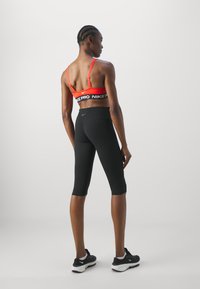 Sujetador deportivo rojo con banda negra "Nike Pro", combinado con leggings negros hasta la rodilla y zapatillas deportivas negras. Tela suave, ajuste atlético.
