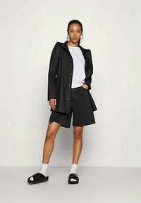 Svart vanntett jakke med hette, over en hvit t-skjorte. Kombinert med svarte denimshorts, hvite sokker og svarte sandaler.