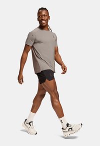 Ljust grå kortärmad träningsskjorta i kombination med svarta shorts. Modellen har på sig vita skor med svarta detaljer och vita strumpor.