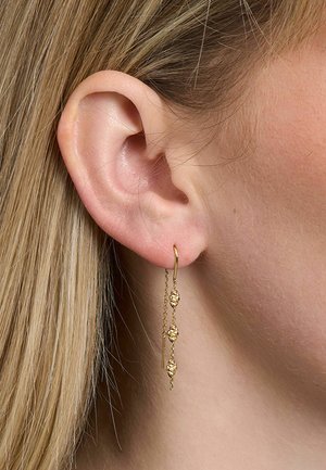 Prim-plan cu o ureche blondă care poartă un cercel delicat auriu atârnat cu trei mărgele texturate pe un lanț subțire.