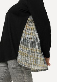 Zwart top met een textuur, geplisseerde, patroonstof inzet in tinten geel, grijs en wit aan de zijkant, gecombineerd met lichtgrijze jeans.