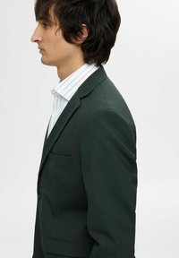 Donkergroene blazer met een gestructureerd ontwerp, enkele knoopsluiting en zijzak. Draag het over een licht gestreept shirt, wat een soepele textuur laat zien.