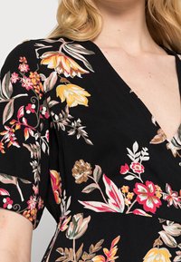 Robe florale noire avec un décolleté en V profond, ornée de fleurs multicolores en rose, jaune et blanc, confectionnée en tissu doux avec des manches courtes.