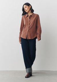 Barna gombos ing hegyes gallérral, bőszárú sötét farmerrel és barna, sarkú csizmával párosítva. Simaságú anyag, laza szabás.