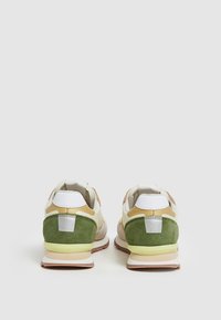 Zapatillas con una parte superior de cuero blanco, talón de ante verde, acentos en color beige y una suela de goma beige. Detalle de hardware reflectante en la parte trasera.