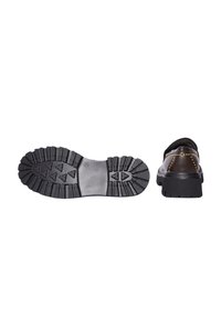 Scarpa slip-on nera con un accento in pelle marrone e dettagli borchiati. Presenta una suola in gomma spessa con un motivo di battistrada robusto.